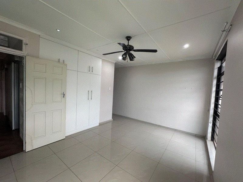A clean, empty bedroom featuring neutral tiled flooring, built-in cupboards, a ceiling fan, and recessed lighting, offering a blank canvas for personalization.