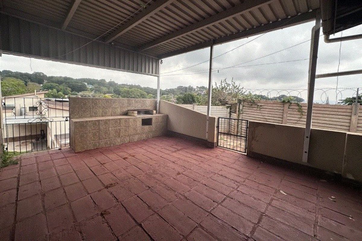 A covered outdoor patio featuring a built-in braai, tiled flooring, and secure perimeter fencing, offering a functional space for outdoor entertainment.