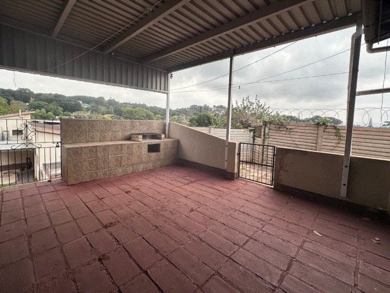A covered outdoor patio featuring a built-in braai, tiled flooring, and secure perimeter fencing, offering a functional space for outdoor entertainment.