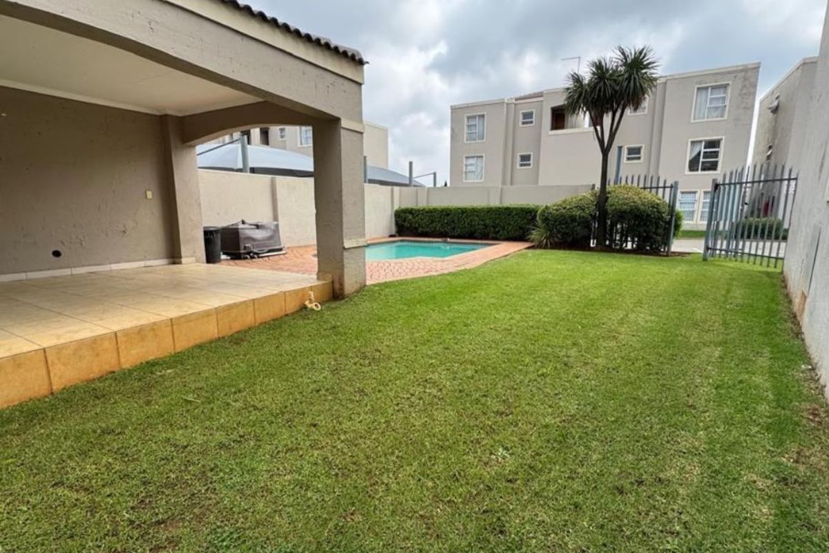 Rear exterior view featuring a covered patio, private swimming pool, paved surround, and a well-maintained lawn area within a secure complex.