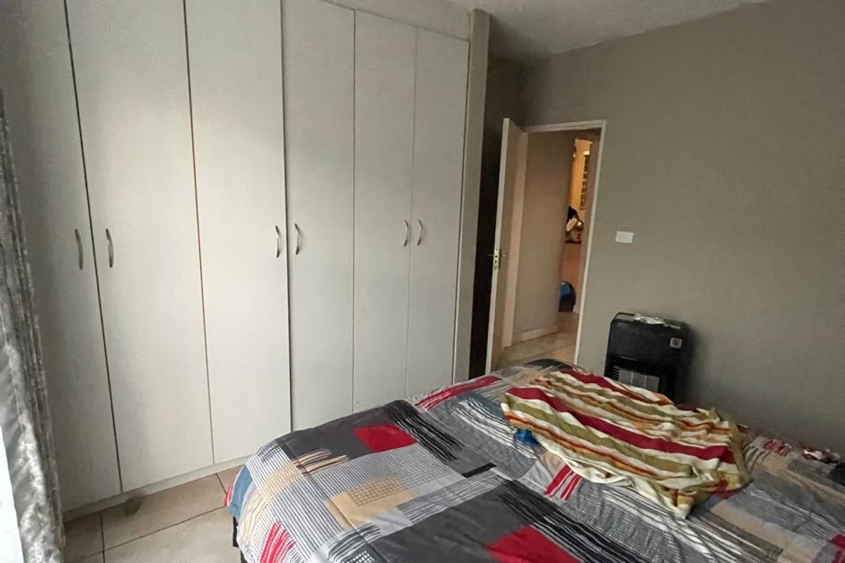 A bedroom featuring built-in cupboards and tiled flooring, currently requiring attention to the ceiling light fixture and exposed electrical wiring.
