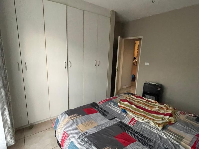 A bedroom featuring built-in cupboards and tiled flooring, currently requiring attention to the ceiling light fixture and exposed electrical wiring.