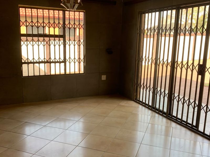 An empty living room featuring tiled flooring, a textured ceiling with decorative cornice, and security gates on the window and sliding door.