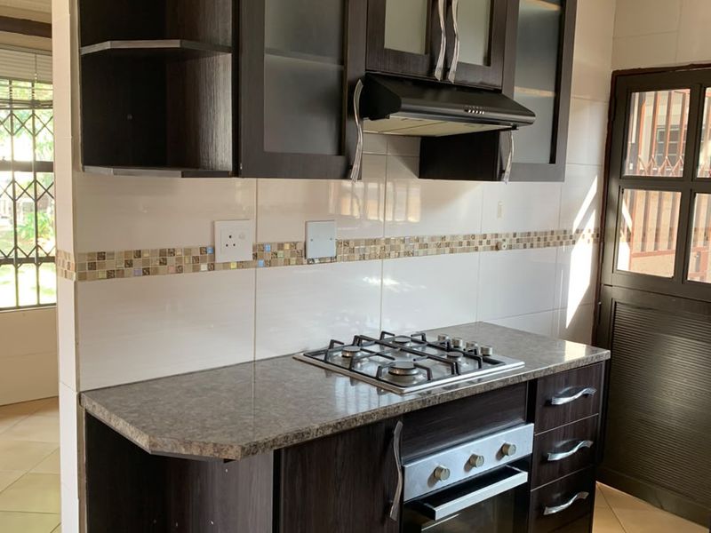 A compact kitchen featuring dark wood cabinetry, granite countertops, a built-in gas hob, oven, and extractor fan with tiled finishes.