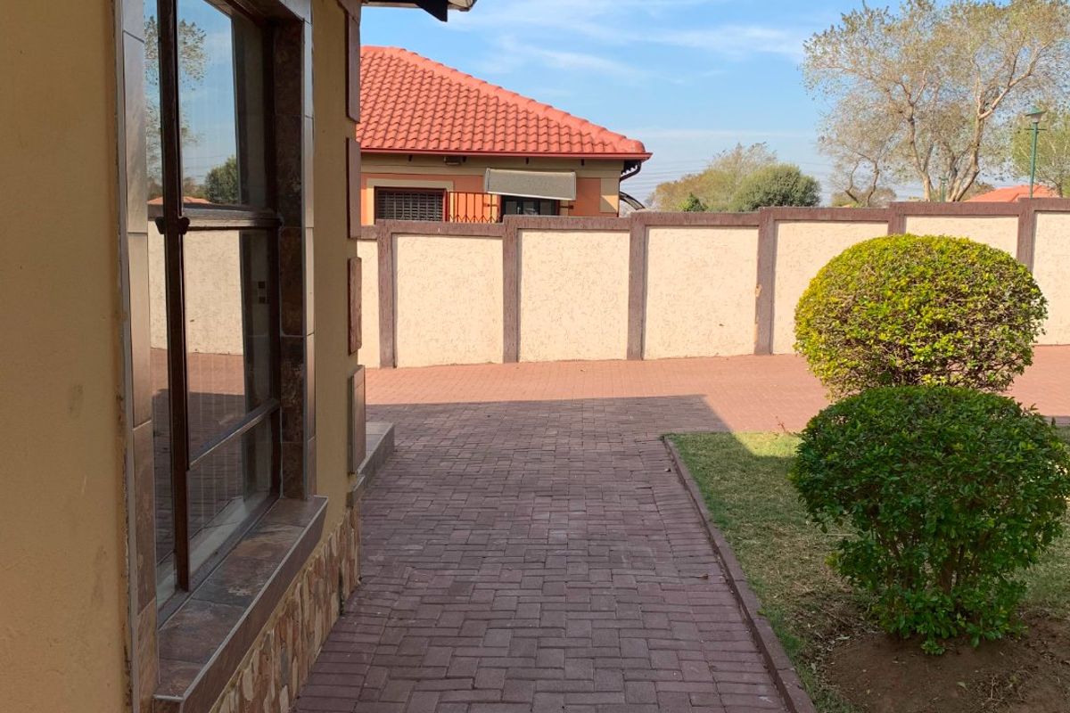 A side view of the property featuring a paved walkway, stone-clad exterior wall, and a secure boundary wall.