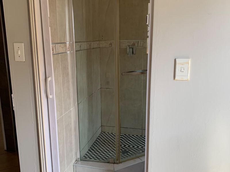 A compact bathroom featuring a corner shower enclosure with tiled walls and flooring, accessed via a sliding door.