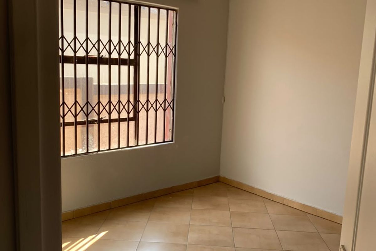 A clean, empty bedroom featuring neutral wall paint, tiled flooring, and security bars on the window.