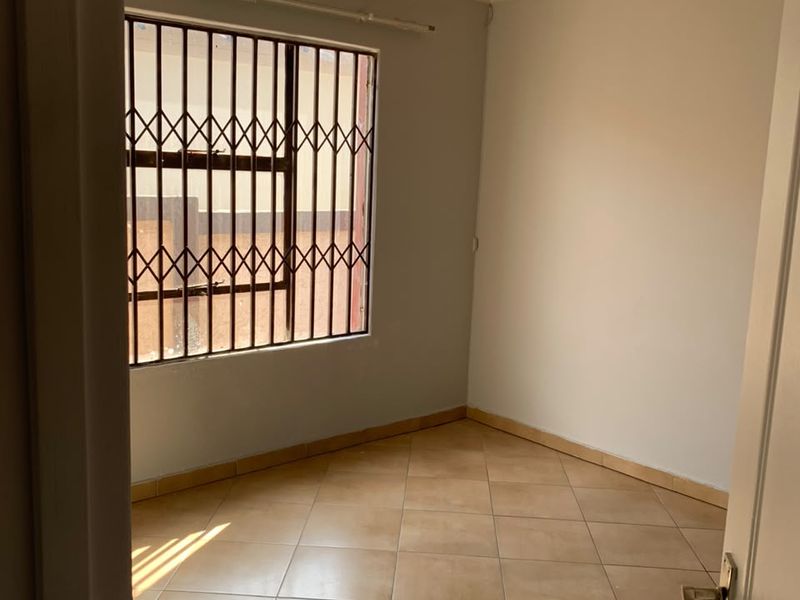 A clean, empty bedroom featuring neutral wall paint, tiled flooring, and security bars on the window.