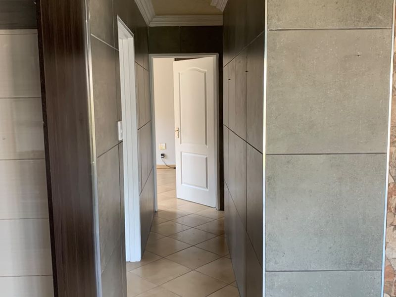 A tiled hallway featuring modern grey wall cladding, recessed downlighting, and decorative ceiling cornicing, leading to an adjacent room.