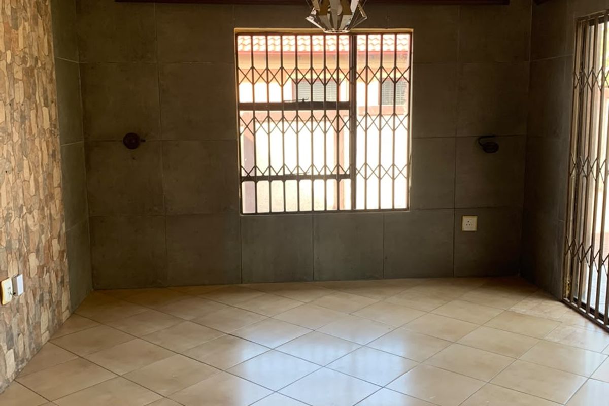 An empty living area featuring tiled floors, a textured yellow ceiling with a decorative rose, and a stone-clad feature wall with security gates.