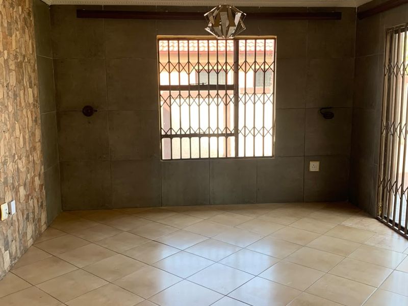 An empty living area featuring tiled floors, a textured yellow ceiling with a decorative rose, and a stone-clad feature wall with security gates.