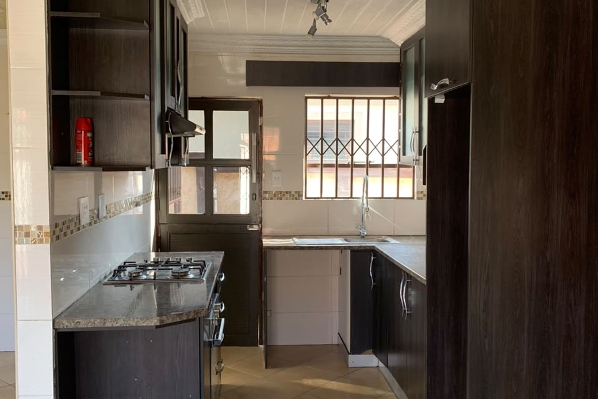 A functional kitchen featuring dark built-in cabinetry, a gas hob, tiled flooring, and a security gate leading to the exterior.