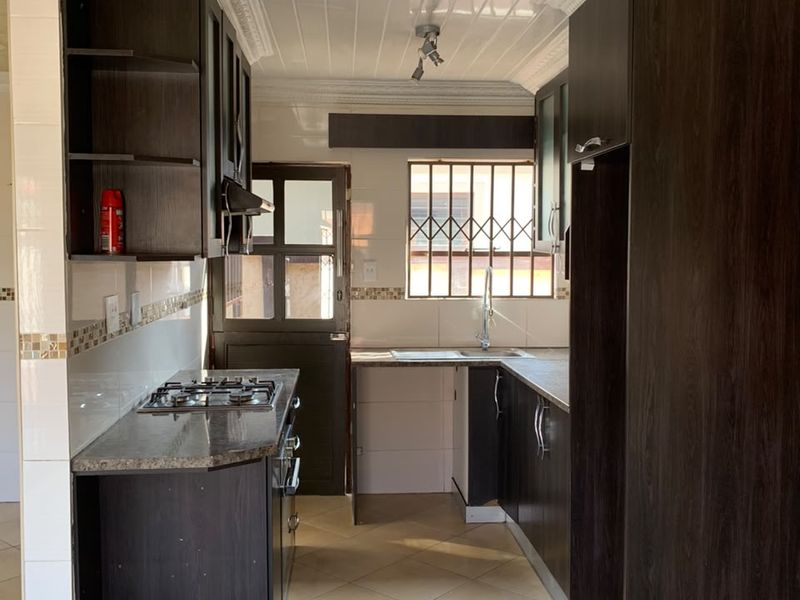 A functional kitchen featuring dark built-in cabinetry, a gas hob, tiled flooring, and a security gate leading to the exterior.