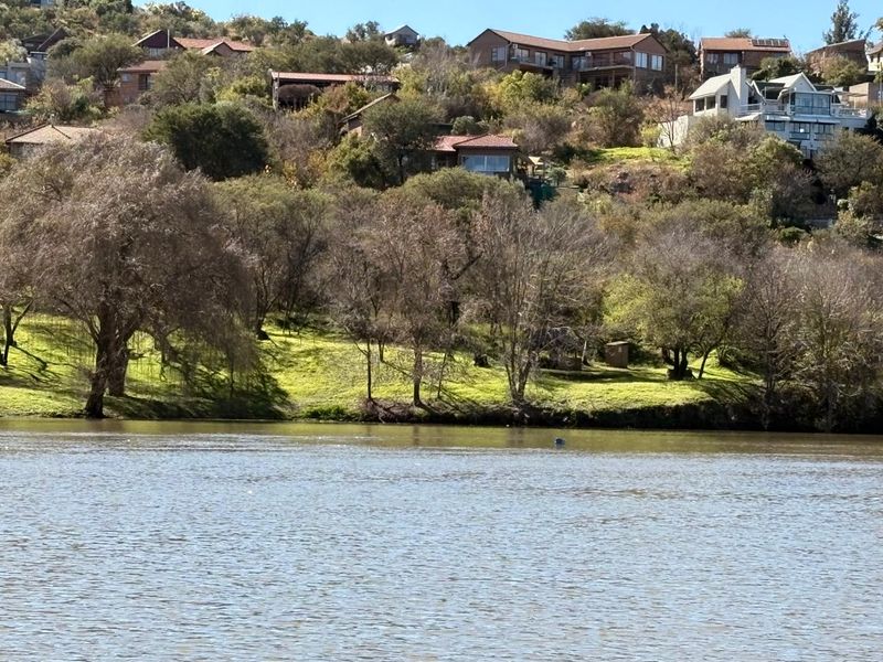 A scenic view of the waterfront property featuring sloped, tree-lined terrain and surrounding residential hillside landscape.