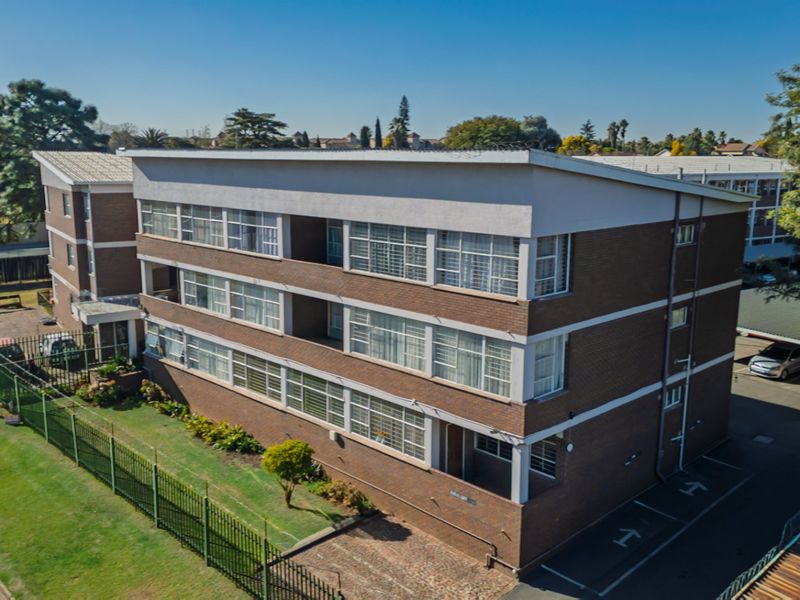 Aerial view of a multi-story brick apartment building featuring a metal roof, surrounding security fencing, and an adjacent paved parking area.