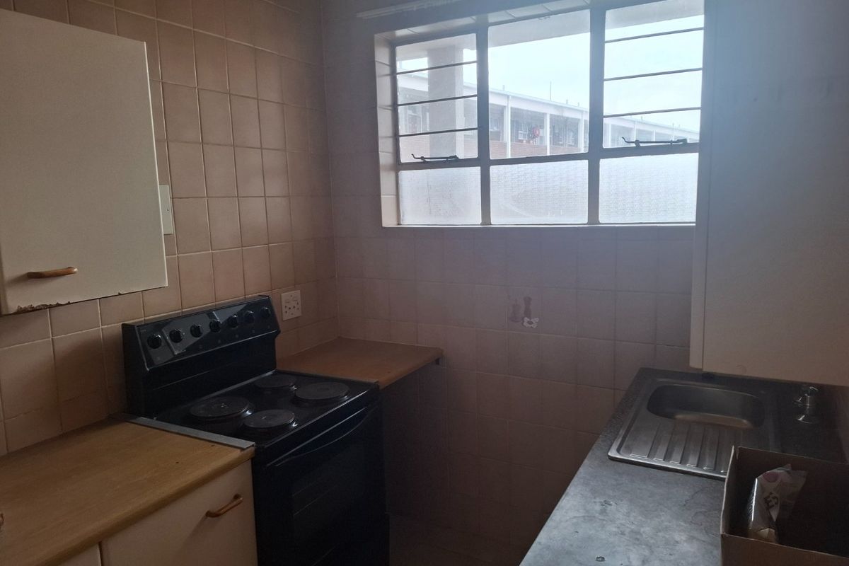 A compact kitchen featuring dated wall tiles, laminate countertops, a stainless steel sink, and a freestanding electric stove.