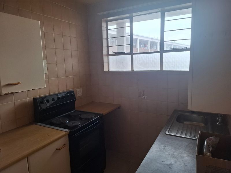 A compact kitchen featuring dated wall tiles, laminate countertops, a stainless steel sink, and a freestanding electric stove.