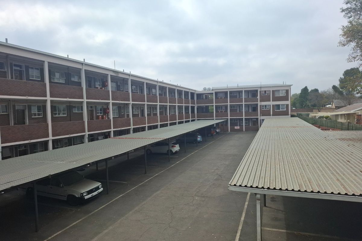 Exterior view of an apartment complex featuring a paved parking area with covered carports and multi-story brick residential units.