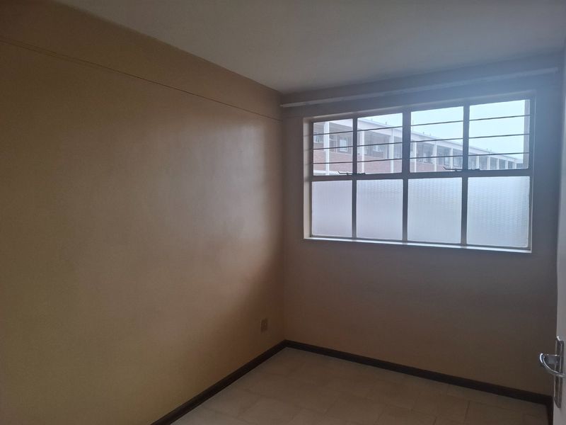 An empty bedroom featuring tiled flooring and a large steel-framed window with frosted glass, offering a blank canvas for renovation.