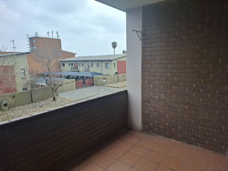 A covered balcony featuring brick walls and tiled flooring, offering an open view of the surrounding apartment complex.