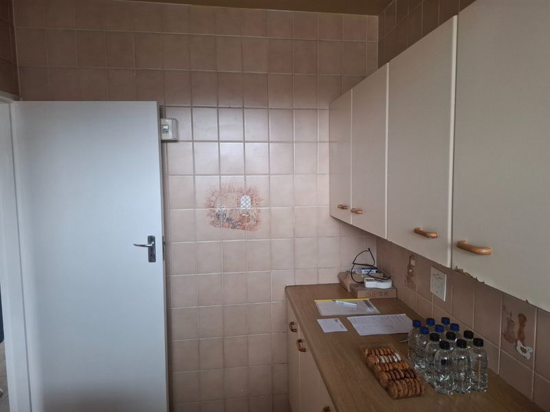 A functional scullery or utility area featuring tiled walls, built-in cabinetry, and laminate countertops, showing signs of wear and dated finishes.