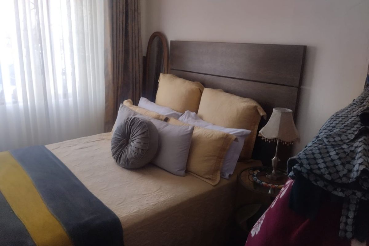 A bedroom featuring a built-in headboard and large window with curtains, providing natural light to the space.