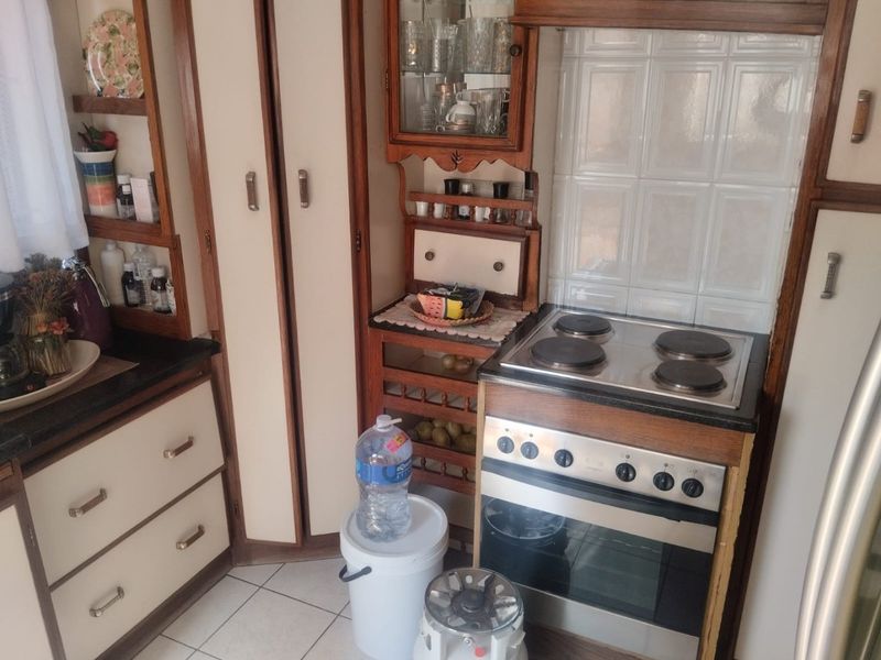 A compact kitchen featuring dated wooden cabinetry, a built-in electric stove and oven, and tiled backsplash.