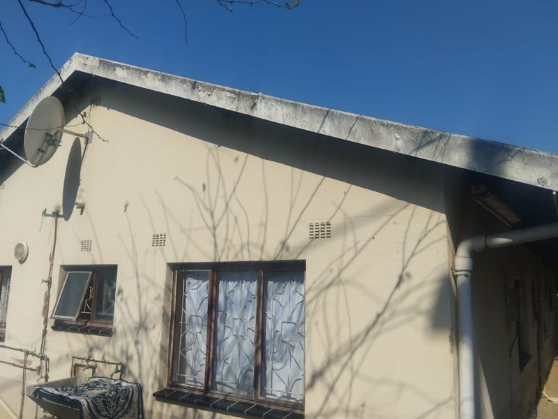 Rear exterior view of the house showing weathered fascia, security bars on windows, and external plumbing fixtures.