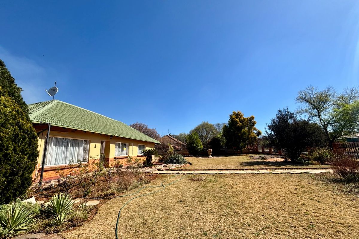 A spacious rear garden featuring a well-maintained brick house with a tiled roof, large windows, and an established lawn area.