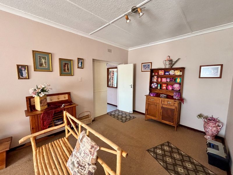 A living room featuring carpeted flooring, ceiling coving, and track lighting, showing signs of wear with visible cracks in the ceiling panels.