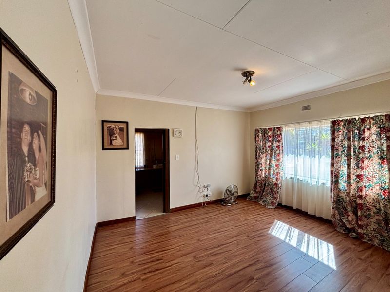 A spacious living room featuring laminate flooring, neutral walls, and a large window, offering a blank canvas for interior design updates.