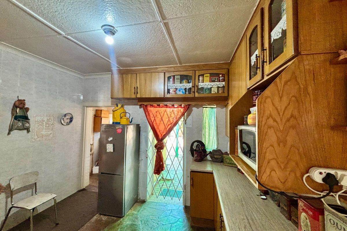 A dated kitchen featuring wooden cabinetry, laminate countertops, and tiled wall finishes, providing a functional space with potential for modern renovation.