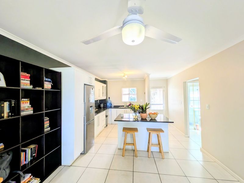 A bright, open-plan kitchen featuring a central island with granite countertops, white cabinetry, and tiled flooring, providing a functional and well-lit cooking space.