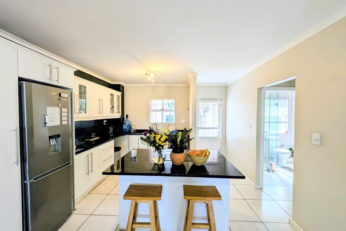 A well-maintained kitchen featuring a central island with granite countertops, white cabinetry, and tiled flooring, with an adjacent view into the bathroom.