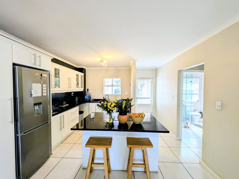A well-maintained kitchen featuring a central island with granite countertops, white cabinetry, and tiled flooring, with an adjacent view into the bathroom.