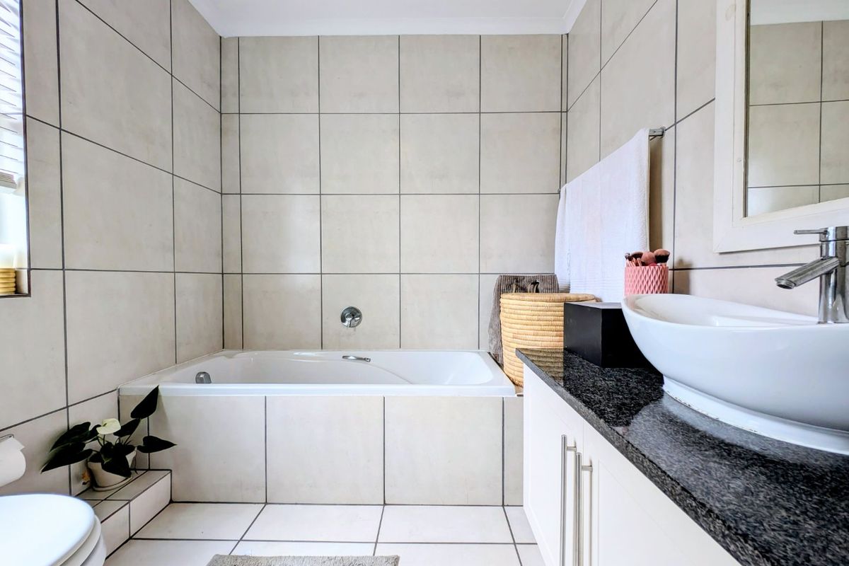 A clean, modern bathroom featuring a built-in bathtub, a granite-topped vanity with a vessel sink, and neutral floor-to-ceiling ceramic tiling.