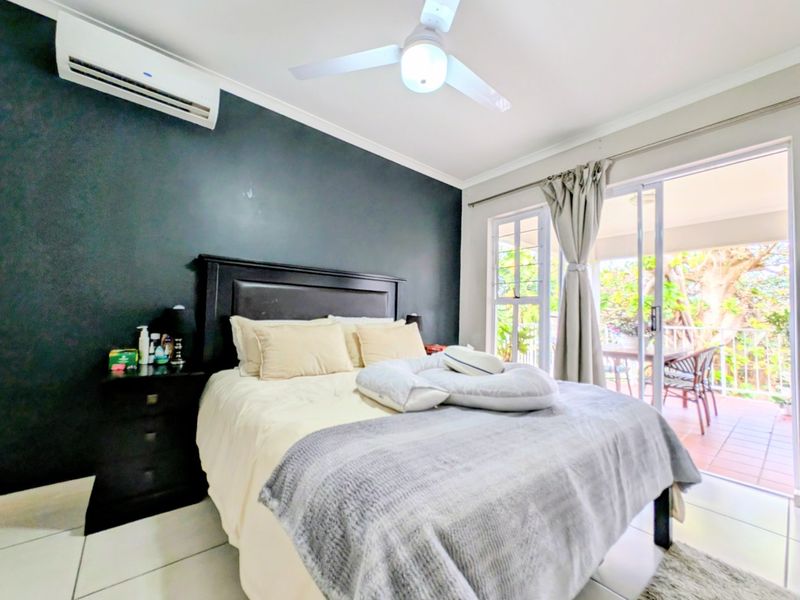 A well-lit bedroom featuring tiled floors, a ceiling fan, split-system air conditioning, and direct access to an outdoor balcony through sliding glass doors.