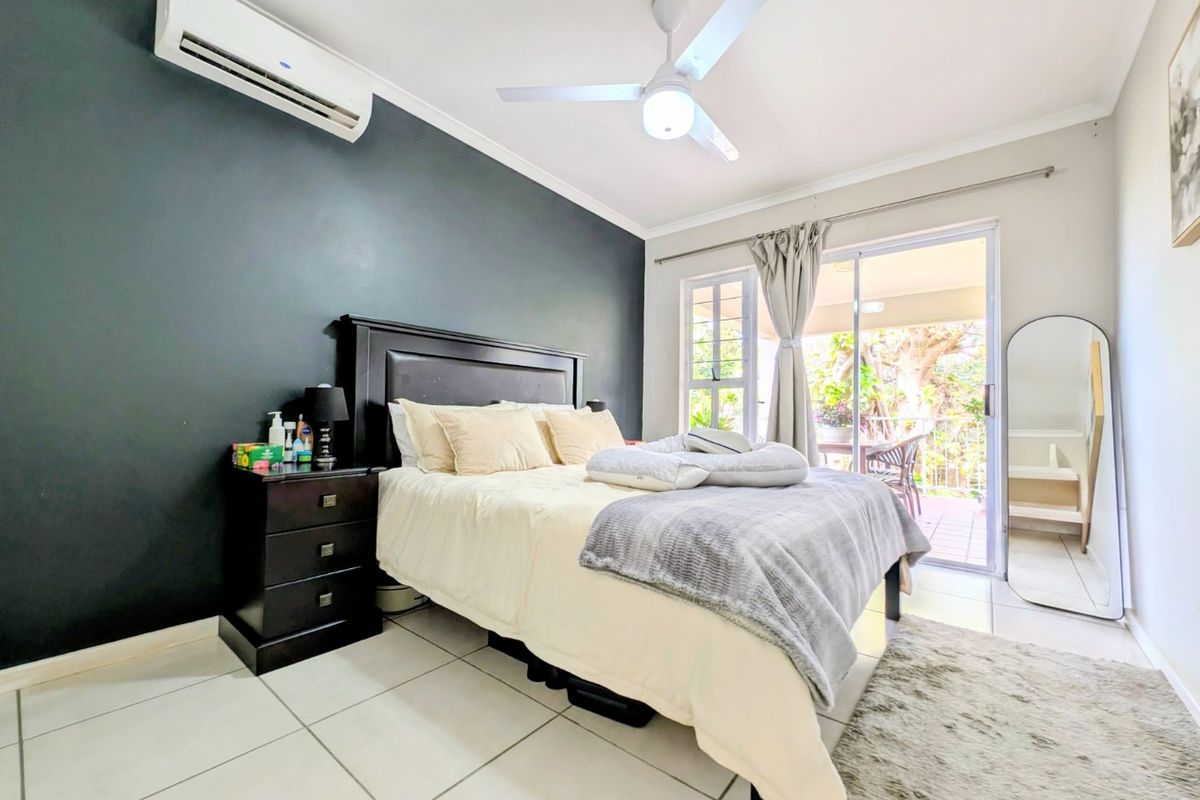 A well-lit bedroom featuring tiled flooring, a ceiling fan, a split-system air conditioner, and sliding glass doors providing access to an outdoor patio area.