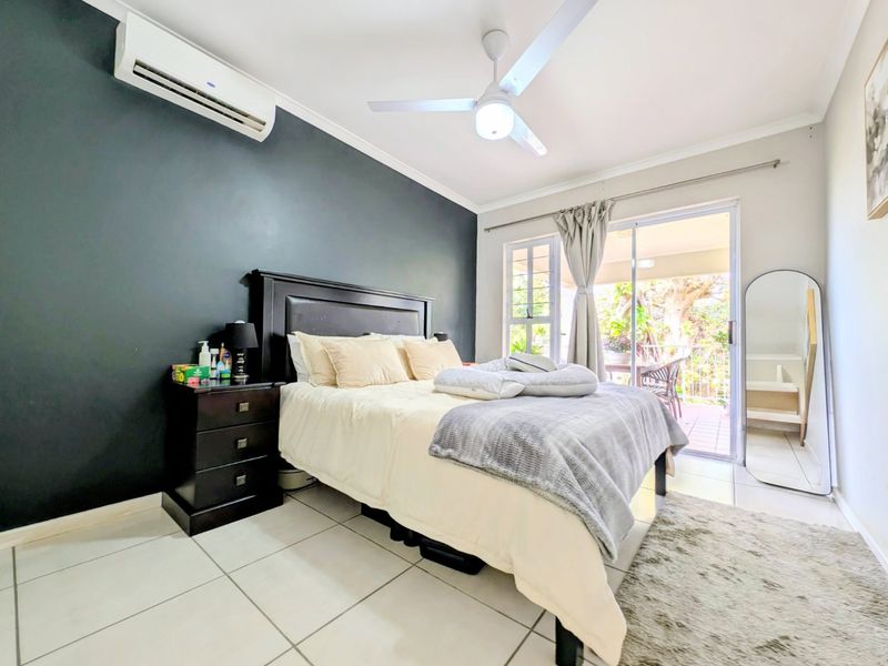 A well-lit bedroom featuring tiled flooring, a ceiling fan, a split-system air conditioner, and sliding glass doors providing access to an outdoor patio area.