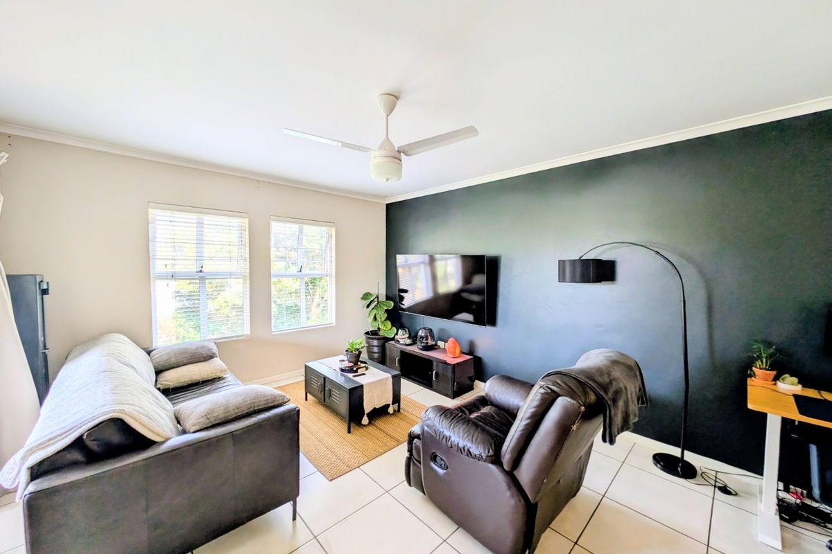A well-lit living room featuring tiled flooring, a ceiling fan, and a dark accent wall, creating a comfortable and modern living space.