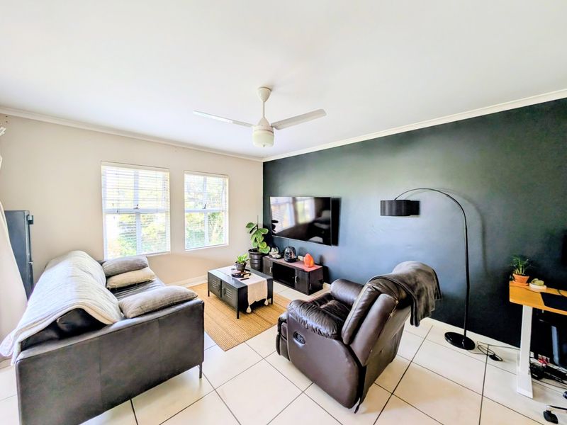 A well-lit living room featuring tiled flooring, a ceiling fan, and a dark accent wall, creating a comfortable and modern living space.