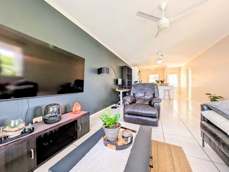 Open plan living area featuring tiled flooring, a dark accent wall, and ceiling fans, flowing into the kitchen space.