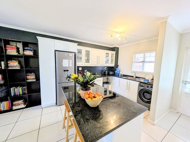 Modern kitchen featuring a granite-topped island, ample built-in cabinetry, integrated hob, and tiled flooring, offering a functional and well-organized culinary space.