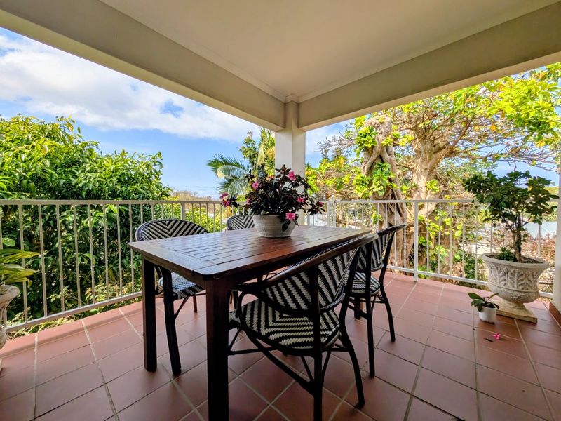 A covered balcony featuring tiled flooring and a white metal balustrade, offering an outdoor space with views of surrounding trees.