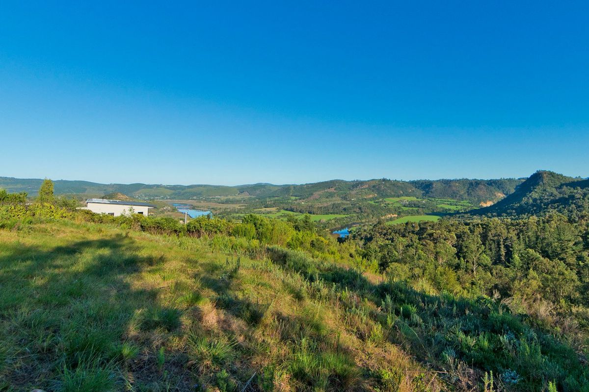 A scenic elevated view overlooking a lush green valley, rolling hills, and a winding river, showcasing the natural beauty of the residential land.