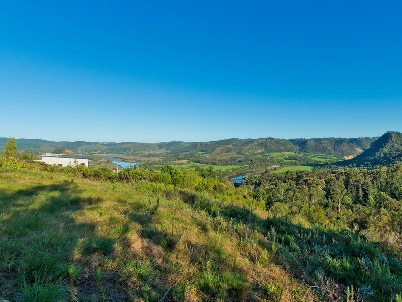 A scenic elevated view overlooking a lush green valley, rolling hills, and a winding river, showcasing the natural beauty of the residential land.
