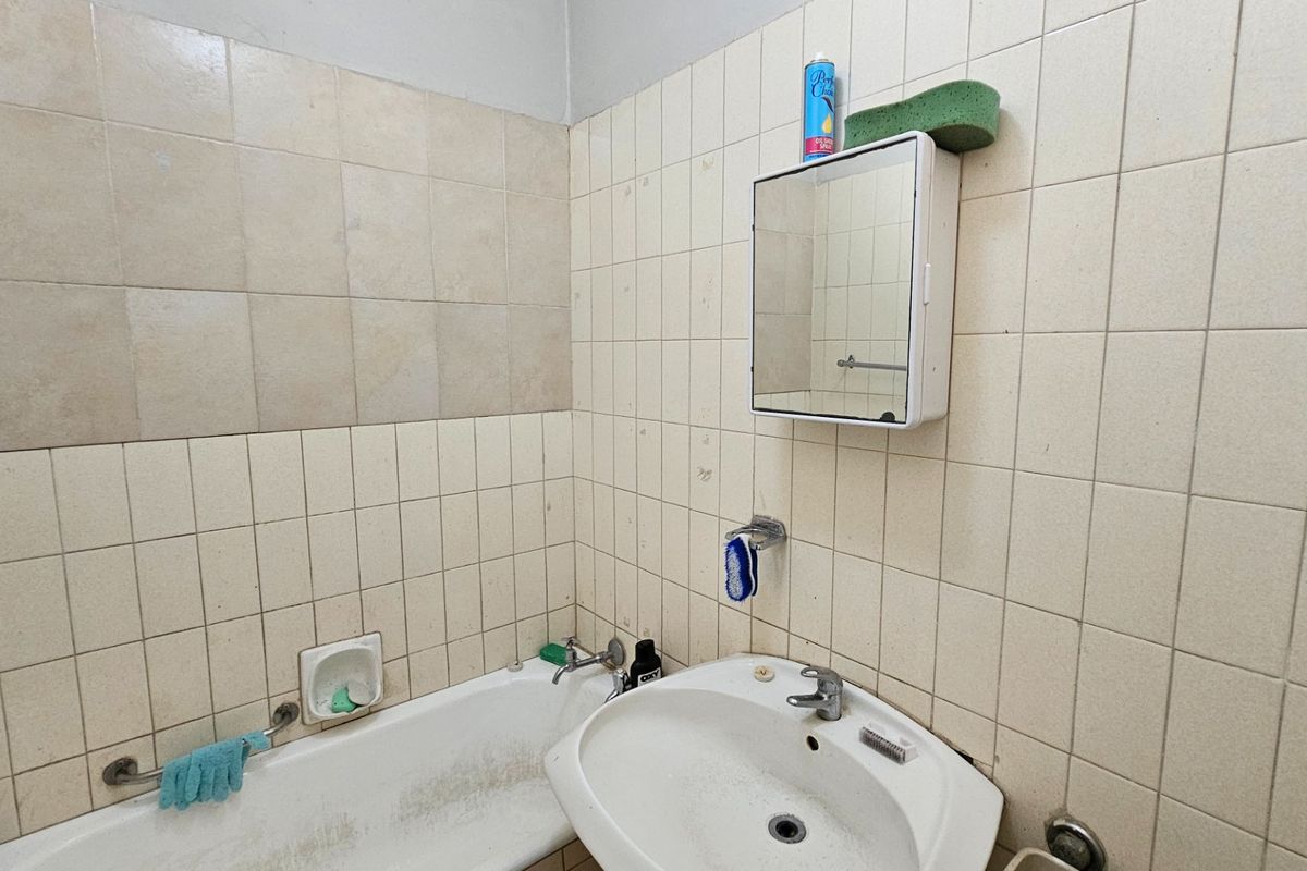 A dated bathroom featuring tiled walls, a pedestal basin, and a bathtub, requiring cosmetic updates to improve its overall condition and appeal.
