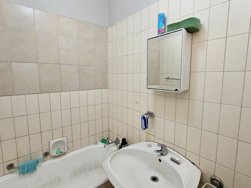 A dated bathroom featuring tiled walls, a pedestal basin, and a bathtub, requiring cosmetic updates to improve its overall condition and appeal.