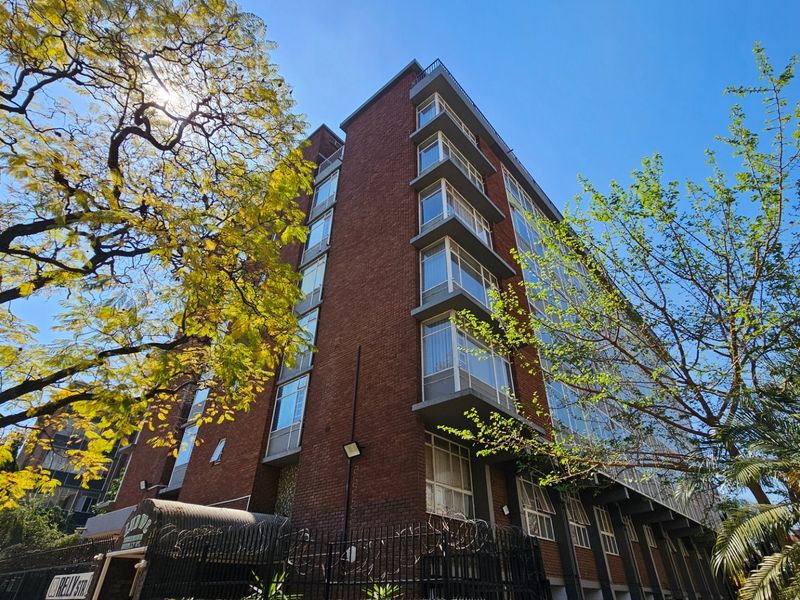 A multi-story commercial building featuring a classic red brick facade with extensive window glazing and perimeter security fencing.