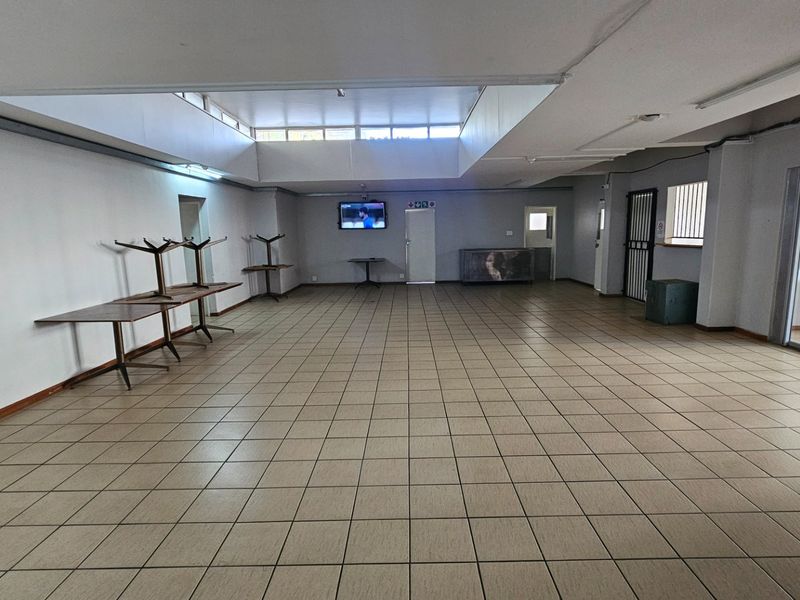 A spacious, open-plan commercial area featuring tiled flooring, recessed ceiling lighting, and a security gate, suitable for various business or office configurations.